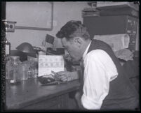 Police sergeant H. L. Barlow inspects fingerprints on a mirror, in an effort to solve Marion Parker murder case, Los Angeles, 1927-1933