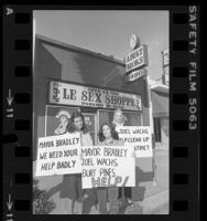 Three women holding signs, one reading "Joel Wachs Help Clean Up Our District," in front of 24-hour "Le Sex Shoppe" in Los Angeles, Calif., 1980