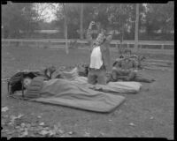 Boy Scouts with sleeping bags at a camping event in a park, circa 1935