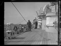 A sailor with a broom and a civilian on the deck of a US Navy battleship