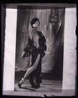 Performer Billye Beck posing beside a birdcage and wearing a revealing robe, Los Angeles, circa 1924