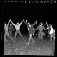 Seven men with arms up in unity being marched off by police during Isla Vista riots near UC Santa Barbara, 1970