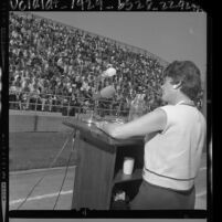 Dorothy Healey podium speaking to crowd in bleachers at Cal State Los Angeles, 1964