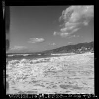 Waves breaking on beach with cliffs and buildings in distance near Santa Monica, Calif., 1964