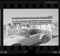 Group portrait of race car drivers around Porsche Carrera at Riverside International Raceway, Riverside, Calif., 1973