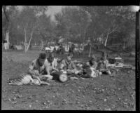 Boy Scouts make feathered headgear at a camping event in a park, circa 1935