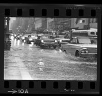 Automobiles driving through flooded streets at Broadway and 7th Street in downtown Los Angeles, Calif., 1965