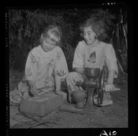 Betsy Brown, right, grinds maize while Susan Wright prepares it for cooking, 1958