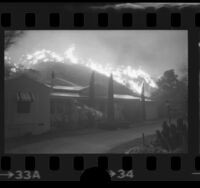 Man watering down roof of house as wildfire burns on hill behind house in Lake View Terrace, Calif., 1975