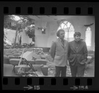 Reverend Troy Perry and Jerry Small standing amid fire damage at Metropolitan Community Church in Los Angeles, Calif., 1973