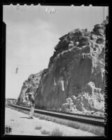 Jim Pahawk, Cherokee Indian stands beneath the great stone face he discovered in cliffs in Victor Valley, Calif., 1948