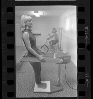 Women using exercise bike and vibrator belt in gym of their Los Angeles apartment complex, 1967