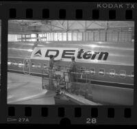 Workers applying "Delta" decal over "Western" decal on a 737 airplane, Calif., 1987