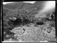 Two destroyed automobiles and 2 men exploring flood damage after the failure of the Saint Francis Dam and resulting cataclysmic flood, San Francisquito Canyon (Calif.), 1928