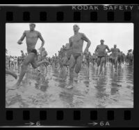 Athletes in swimsuits sprinting along beach at start of the Bud Light U.S. Triathlon Series in Long Beach, Calif., 1984