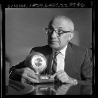 Fred G. Burg of Burgmaster Corp. displaying clock he invented that gives time for 166 cities around the world, 1965