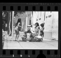 Youngsters playing in wading pool on sidewalk during heat wave in Los Angeles, Calif., 1976