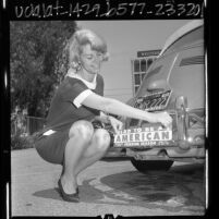 Lynda Morgan, Miss Freedom Season, placing bumper sticker "Glad to Be An American" on car in Woodland Hills, Calif., 1966