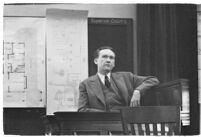 Murder suspect Robert S. James sitting on the witness stand with a plan of his house behind him, Los Angeles, 1936