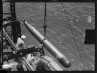 Torpedo suspended above the ocean by a cable next to a ship or dock