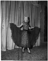 Woman models a black lace dress and gloves during a fashion show, Los Angeles