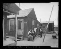 Couple sitting besides a California State Emergency Relief Administration plank board house, circa 1935