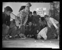 Boys playing in marbles tournament, one with sign reading "No Cameras Please," 1950