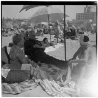 Two women and a man have a picnic under umbrellas at the beach on Labor Day, Los Angeles, September 3, 1945