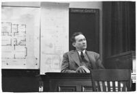 Murder suspect Robert S. James sitting on the witness stand with a plan of his house behind him, Los Angeles, 1936