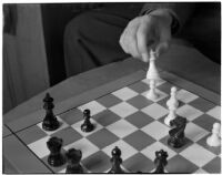 Close-up of a chess board and a player's hand moving the white queen, Los Angeles