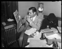 Film actor Clark Gable eating a sandwich and reading a newspaper in an office, Los Angeles, 1937