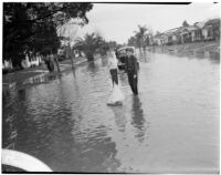 Two boys play with a toy sailboat in a flooded street caused by heavy rainstorms, January 1940