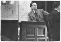 Murder suspect Robert S. James sitting on the witness stand with a plan of his house behind him, Los Angeles, 1936