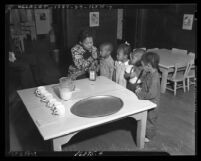 African American woman feeding cod liver oil to four African American children at a Macy Street school, Los Angeles, circa 1938