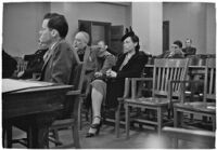 Attorney at table and spectators and witnesses seated behind him during unidentified hearing in courtroom with model cars on table