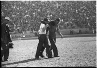 Injured Loyola Lions football player being helped across the field at the Coliseum, Los Angeles, 1937