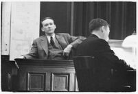 Murder suspect Robert S. James sitting on the witness stand with a plan of his house behind him, Los Angeles, 1936