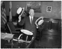 Mayor Frank L. Shaw decides between a bowler hat and a straw hat in his office, Los Angeles, 1930s