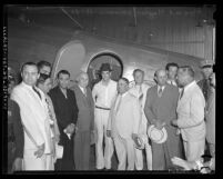 Howard Hughes and group of men standing beside airplane upon Hughes arrival in Los Angeles on August 2, 1938