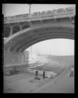 Two policemen standing over body of man who jumped from First Street Bridge, as crowd watches from bridge Los Angeles, circa 1948