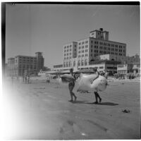 Two women on the beach carry large inflatables toward the water on Labor Day, Los Angeles, September 3, 1945