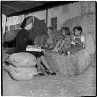 Mrs. Rosita Yacopi talks to three young children sitting on a hay bale at the Shrine Charity Circus, Los Angeles, June 1946