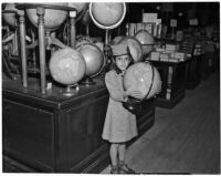 Young girl stands holding a globe in a shop, Los Angeles, 1937