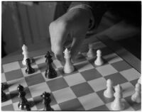 Close-up of a chess board and a player's hand moving the white queen, Los Angeles