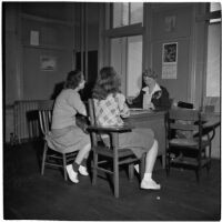 Mrs. Mallie Kerr sits at her desk across from two teenage girls, Los Angeles, 1946