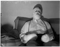 Joe Schrank sits on a couch with his hands and face completely wrapped in bandages, Los Angeles