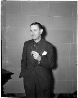 Thomas W. Hall stands by a staircase wearing a suit, Los Angeles, 1930s