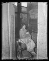 Woman seated on bed holding child on her lap in slums of Los Angeles, 1937
