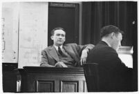 Murder suspect Robert S. James sitting on the witness stand with a plan of his house behind him, Los Angeles, 1936