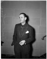 Thomas W. Hall stands by a staircase wearing a suit, Los Angeles, 1930s